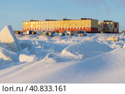 A small coastal settlement in the Far North of Russia. Residential buildings and fishing sheds on the coast of the frozen sea. Cold winter weather. Ice hummocks and snow. Chukotka Autonomous Region. Стоковое фото, фотограф Андрей Степанов / Фотобанк Лори