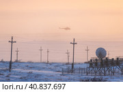 Industrial arctic landscape. A helicopter is landing at an airstrip in the tundra in the Arctic. Polar aviation. Cold frosty and windy winter weather. Bad visibility. Satellite dish and electric poles. Стоковое фото, фотограф Андрей Степанов / Фотобанк Лори