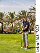 Young man golfer standing on golf course in sportswear and sunglasses, teeing golf club training at palm trees background. Healthy sports lifestyle and leisure activity concept. Copy ad text space. Стоковое фото, фотограф Aleksandr Golubev / Фотобанк Лори