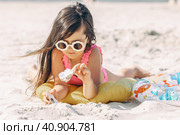 Happy cute smiling little girl in sunglasses lying on the sand on a beach in a swimsuit. Summer concept. Стоковое фото, фотограф Ирина Михайличенко / Фотобанк Лори