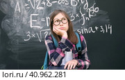 Teen girl little student in glasses and blue backpack standing and thinking on chalkboard background. Then she is pointing up with finger because finds answer. Brainstorming and Bright idea concept. Стоковое видео, видеограф Марина Демидюк / Фотобанк Лори