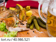 Fried chicken wings served on a wooden Board with Idaho potatoes, pickled gherkins and fresh lettuce leaves. A mug of beer is next to it. жареные куриные крылышки подаются на деревянной доске с картофелем Айдахо, маринованными корнишонами и свежими листьями салата. Рядом с ним стоит кружка пива. Стоковое фото, фотограф Дмитрий Березнев / Фотобанк Лори
