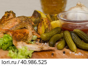 Fried chicken wings served on a wooden Board with Idaho potatoes, pickled gherkins and fresh lettuce leaves. A mug of beer is next to it. жареные куриные крылышки подаются на деревянной доске с картофелем Айдахо, маринованными корнишонами и свежими листьями салата. Рядом с ним стоит кружка пива. Стоковое фото, фотограф Дмитрий Березнев / Фотобанк Лори