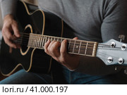 Playing the guitar. Strumming acoustic guitar. Musician plays music. Man fingers holding mediator. Man hand playing guitar neck in dark room. Unrecognizable person rehearsing, fretboard close-up. Стоковое фото, фотограф Марина Демидюк / Фотобанк Лори
