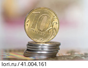 Деньги. Монета номиналом в 10 рублей на стопке монет в 1 рубль на фоне 100-рублевых купюр. Стоковое фото, фотограф E. O. / Фотобанк Лори