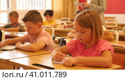 Diligent tweens studying in classroom, listening to lecturer and writing in notebooks. Стоковое видео, видеограф Яков Филимонов / Фотобанк Лори