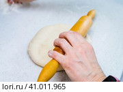 Woman's hands with a dough. A woman rolls out a piece of dough with a wooden rolling pin. She takes a pinch of flour by another hand. Женские руки с тестом. Женщина раскатывает кусок теста деревянной скалкой. Другой рукой она берет щепотку муки. Стоковое фото, фотограф Дмитрий Березнев / Фотобанк Лори
