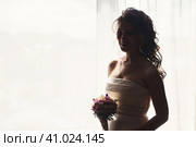 Silhouette of bride lady in wedding dress with nice bouquet at window, looking at camera. Sensual lovely woman fiancee posing in shadow. Concept of luxury wed fashionable style. Copy ad text space. Стоковое фото, фотограф Aleksandr Golubev / Фотобанк Лори