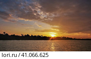 Bright dramatic sunset over the river. There are purple clouds in the sky. Golden rays of the sun over the horizon. Sunny path on the water. Tropical thickets on the shore. Zambezi. Zimbabwe. Стоковое фото, фотограф Вера Ивановна Кубарева / Фотобанк Лори