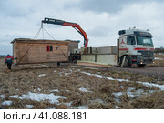 Разгрузка краном-манипулятором строительной бытовки на сельском участке для обустройства стройплощадки. Ленинградская область (2021 год). Редакционное фото, фотограф Виктор Карасев / Фотобанк Лори