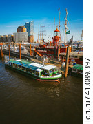 Hamburg, Germany - May 17, 2018: HafenCity, Speicherstadt: Panoramic view of Red fire patrol boat with a restaurant on the board. The modern Elbphilharmonie building in the background. Редакционное фото, фотограф Igor Tichonow / Фотобанк Лори