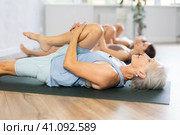 Elderly woman performing stretching Ardha Pawanmuktasana in yoga studio. Стоковое фото, фотограф Яков Филимонов / Фотобанк Лори