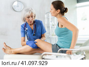 Woman client of clinic looks at specialist and tells to mature woman doctor where knee hurts. Стоковое фото, фотограф Яков Филимонов / Фотобанк Лори