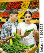 Young family couple chooses fresh bitter melon (Momordica charantia) in grocery supermarket. Стоковое фото, фотограф Яков Филимонов / Фотобанк Лори