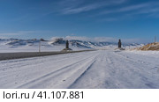 An asphalt road runs through a snow-covered valley. There are figures of idols on the roadsides. Ahead is a mountain range against the blue sky. Perspective. Altai. Chuysky tract. Стоковое фото, фотограф Вера Ивановна Кубарева / Фотобанк Лори