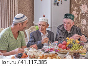 Local residents of Siberian village celebrate Muslim holiday Kurban Bayram at their home table. Mullah talking with villagers. Eid al-Adha (2021 год). Редакционное фото, фотограф Ирина Кононова / Фотобанк Лори
