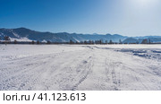 The snow in the valley is well trampled. Tire tracks are everywhere. The forest is visible in the distance. A picturesque mountain range against a clear blue sky. Copy space. Altai. Стоковое фото, фотограф Вера Ивановна Кубарева / Фотобанк Лори