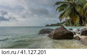 Picturesque boulders lie in the water near the ocean shore. Foam waves all around. Leaning palm trees against the sky and clouds. Seychelles. Mahe. Стоковое фото, фотограф Вера Ивановна Кубарева / Фотобанк Лори