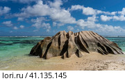 A bizarre granite boulder with smoothed folded slopes on the beach of a tropical island. The waves of the turquoise ocean spread over the wet sand. Clouds in the blue sky. Seychelles. La Digue. Стоковое фото, фотограф Вера Ивановна Кубарева / Фотобанк Лори