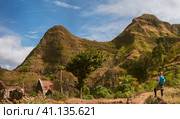 Panoramic view of woman tourist with blue backpack making photo of landscape in Mountains of Santo Antao island, Cabo Verde. Стоковое фото, фотограф Igor Tichonow / Фотобанк Лори