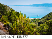 Lonely yacht on hidden Fteri beach lagoon, Kefalonia, Greece. Framed view between pine tree branches during trekking path down ravine (2018 год). Стоковое фото, фотограф Igor Tichonow / Фотобанк Лори