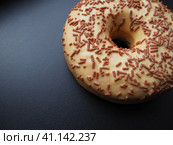 A doughnut or donut. A type of leavened fried dough. Sweet snack that can be homemade or purchased in bakeries, supermarkets, food stalls. Delicious pie with light icing on black or gray background. Стоковое фото, фотограф Юлия Петровская / Фотобанк Лори