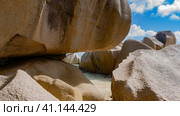 Huge granite boulders are piled on the sandy beach. Bizarre outlines, smoothed slopes. Through the openings you can see the ocean, the blue sky with clouds. Seychelles. La Digue. (2022 год). Стоковое фото, фотограф Вера Ивановна Кубарева / Фотобанк Лори