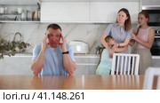 Irritated dissatisfied woman yelling at confused husband in home kitchen. Two frustrated teenage girls sitting at table during parental quarrel, selective focus. Стоковое видео, видеограф Яков Филимонов / Фотобанк Лори