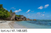Picturesque granite boulders and rocks with steep smoothed slopes on a tropical beach. Turquoise ocean waves on the sand. Lush tropical vegetation. Blue sky, clouds. Seychelles. La Digue. (2022 год). Стоковое фото, фотограф Вера Ивановна Кубарева / Фотобанк Лори