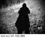 Shadow of a man or woman in a raincoat or coat. Hair bob, arms bent. The shadow falls on a pinch with grass and vegetation. Silhouette of an unknown mysterious person. Halloween theme. Стоковое фото, фотограф Юлия Петровская / Фотобанк Лори