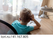unrecognizable first-grade boy can't bring himself to do his homework, daydreaming while staring out window. Procrastination, school workload. Стоковое фото, фотограф Алла Чесноковва / Фотобанк Лори