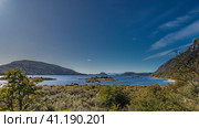 The calm blue lake is surrounded by mountains. A small island in the center of the reservoir. Green vegetation on the banks. Blue sky, light clouds. Lapataia Bay. Tierra del Fuego National Park. Стоковое фото, фотограф Вера Ивановна Кубарева / Фотобанк Лори