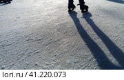 Children ride in a city park on an ice rink. Feet skater while skating on ice. The low winter sun weakly illuminates the ice. Dark shapes and long shadows on the surface. Sports movements. Стоковое фото, фотограф Юлия Петровская / Фотобанк Лори