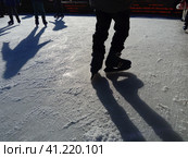 Children ride in a city park on an ice rink. Feet skater while skating on ice. The low winter sun weakly illuminates the ice. Dark shapes and long shadows on the surface. Sports movements. Стоковое фото, фотограф Юлия Петровская / Фотобанк Лори