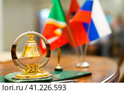 На столе в зале торжественной регистрации брака стоит изделие-символ с золотым свадебным кольцом и колокольчиком внутри. На фоне видны флажки. Стоковое фото, фотограф Сергей Никифоров-Гордеев / Фотобанк Лори