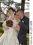 Sremska Mitrovica, Serbia, October 10, 2019 the groom in a gray suit kisses the bride's shoulder in a white dress and a bouquet of red roses. Стоковое фото, фотограф Юлия Петровская / Фотобанк Лори