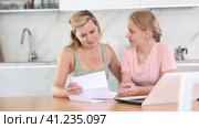Upset teenage girl reading letter about exam results while sitting at home table with concerned mother offering comfort and understanding to daughter. Стоковое видео, видеограф Яков Филимонов / Фотобанк Лори