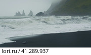 The black sand beach of Reynisfjara with waves hitting the shore on foggy rainy stormy day Vik, Icel. Стоковое видео, видеограф Igor Tichonow / Фотобанк Лори