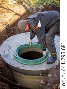 A worker installs a sewer manhole on a septic tank made of concrete rings. Construction of sewage disposal systems for private houses. Стоковое фото, фотограф Коханова Наталья / Фотобанк Лори