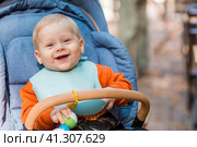 Portrait of a little boy 9 months old in the open air. A happy child in an autumn park is sitting in a stroller. Happy childhood and motherhood. Стоковое фото, фотограф Photojuli / Фотобанк Лори