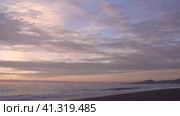 Evening. Sea. The sky is painted in pastel shades of pink and blue. The cape and city buildings are visible in the distance. Waves foaming on a pebble beach. A husky dog runs along the shore and hides. Стоковое видео, видеограф Вера Ивановна Кубарева / Фотобанк Лори