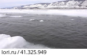 Early spring. On the frozen Lake Baikal, there is a polynya in which ice floes float. Suddenly a piece of ice falls into the water, large transparent splashes. The background is a snowy mountain range. Стоковое видео, видеограф Вера Ивановна Кубарева / Фотобанк Лори
