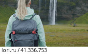 Rear close up view of woman with Seljalandsfoss waterfall Iceland in background. Стоковое видео, видеограф Igor Tichonow / Фотобанк Лори