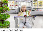 Shocked suprised adorable toddler girl sitting in the shopping cart in a food store or a supermarket. Little kid going shopping. Healthy food for kids. Стоковое фото, фотограф Ирина Михайличенко / Фотобанк Лори