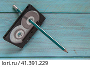 On a blue wooden background is an audio tape with a pencil threaded through it. Стоковое фото, фотограф Воловодов Владимир / Фотобанк Лори