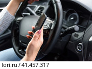 Young woman in jeans and blue sweater is driving the car with one hand, using her smartphone by another hand. Extremely unsafety and risky driving. Молодая женщина в джинсах и синем свитере ведет машину одной рукой, другой рукой пользуется смартфоном. Крайне небезопасное и рискованное вождение. Стоковое фото, фотограф Дмитрий Березнев / Фотобанк Лори