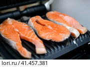 Three raw salmon steaks are toasted on a modern electric non-stick coating grill. Healthy eating concept. Close up photo with selective focus. Три стейка из сырого лосося поджариваются на современном электрическом гриле с антипригарным покрытием. Концепция здорового питания. Фотография крупным планом с выборочным фокусом. Стоковое фото, фотограф Дмитрий Березнев / Фотобанк Лори