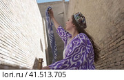 A young woman with long flowing hair, in an oriental robe and skullcap, holds an Asian saber against the backdrop of an ancient city. Slow Motion. Стоковое видео, видеограф Aleksey Kidisyuk / Фотобанк Лори