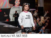 Девочка демонстрирует одежду из коллекции российского бренда Lucky child на подиуме фестиваля детской моды KIDS FASHION WEEK в "Центральном детском магазине на Лубянке" (ЦДМ) в Москве, Россия (2023 год). Редакционное фото, фотограф Николай Винокуров / Фотобанк Лори