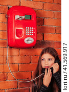 Shocked child girl in leather jacket holding handset call old red payphone on brick wall, looking away. Adorable kid lady model posing with telephone. Support communicate concept. Copy ad text space. Стоковое фото, фотограф Aleksandr Golubev / Фотобанк Лори